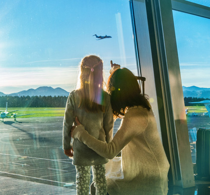 Mutter und Tochter beobachten ein startendes Flugzeug vom Flughafengebäude aus, Sustainable Aviation Fuel (Foto)